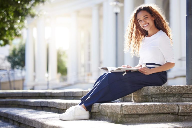 Une jeune femme lit, assise sur des marches au soleil